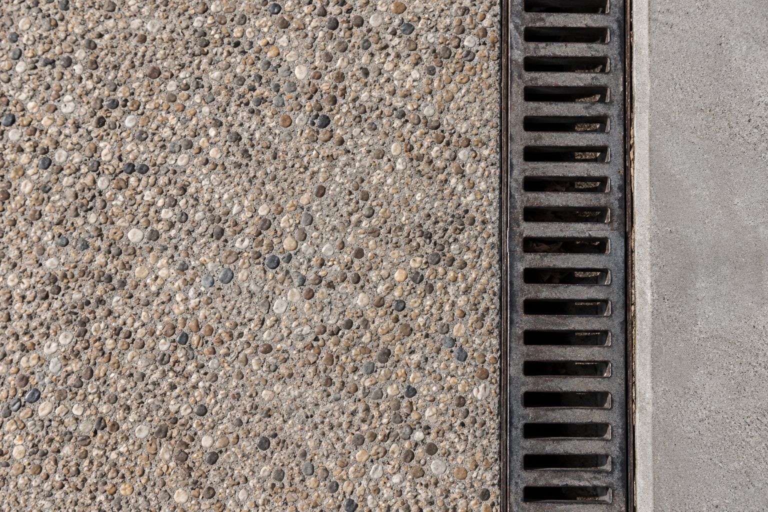Lightly exposed aggregate concrete beside a smooth band and a discreet drain grate