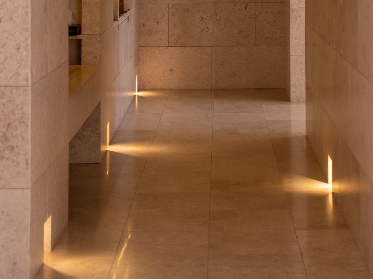 Warm recessed lighting highlights stone niches and the floor of an architectural corridor