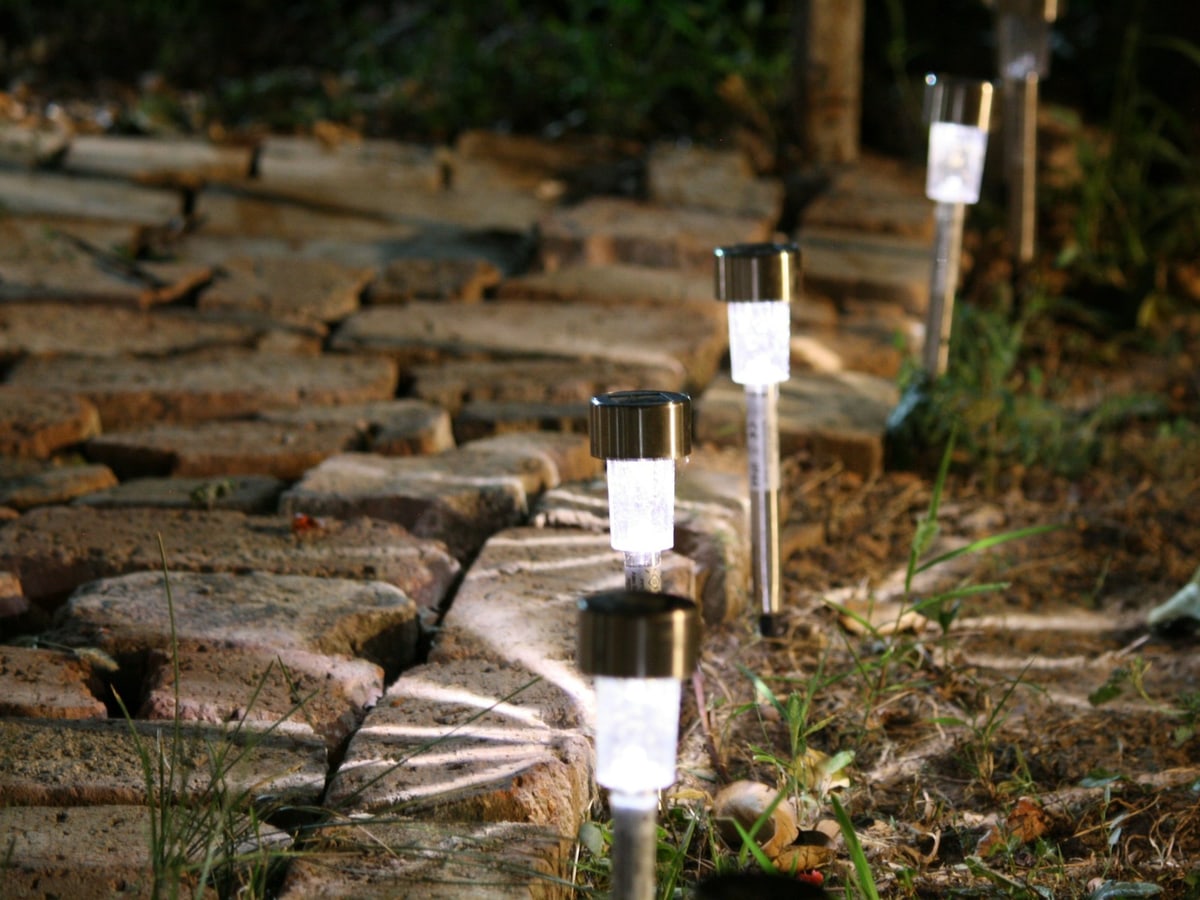 A row of small garden lights illuminates the edge of a stone pathway after dark