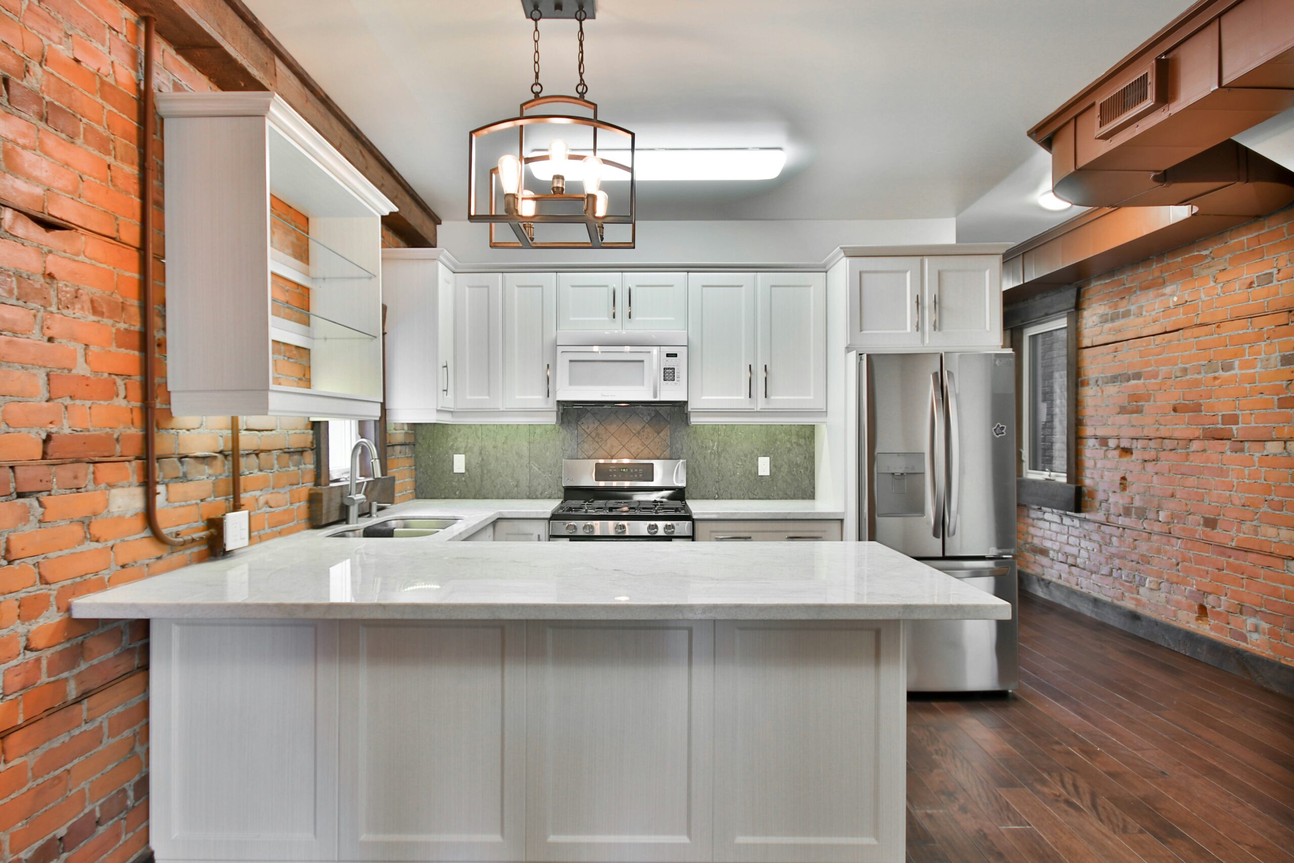 Modern kitchen with white cabinetry, stainless steel appliances, and a central island with a white marble countertop, set against exposed brick walls for a stylish contrast.