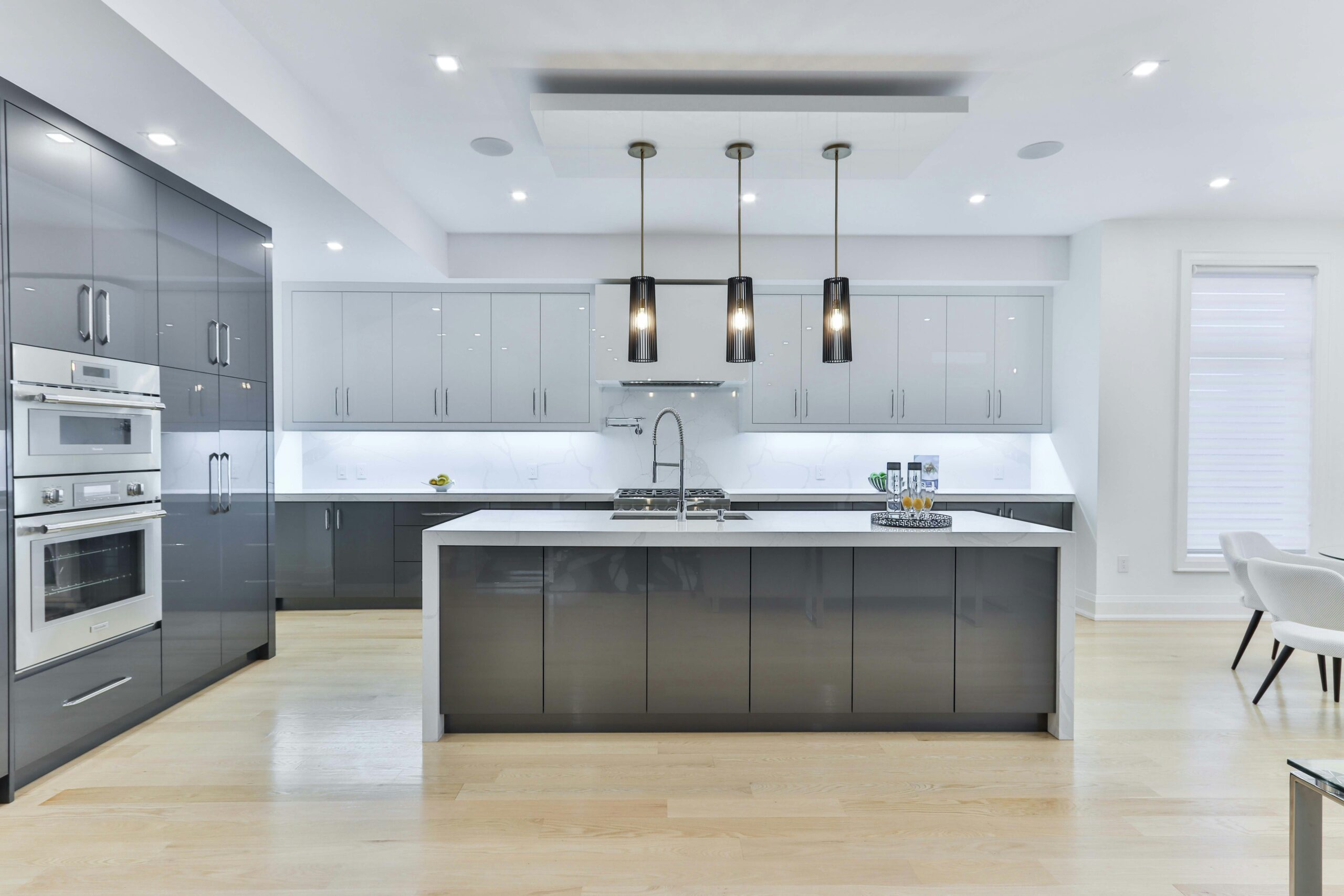 Large modern kitchen with grey cabinetry and white quartz countertops, pendant lighting over a central island, and built-in stainless steel appliances, creating a sleek, contemporary space.